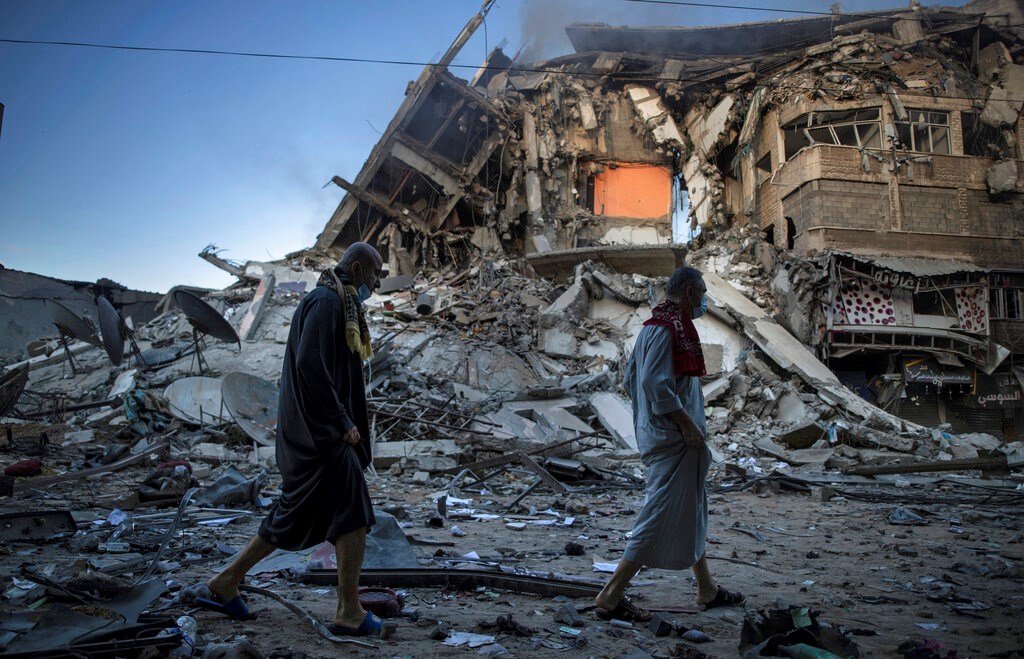 Palestinians walk next to the remains of a destroyed 15-story building hit by Israeli airstrikes on Gaza City on May 13, 2021.