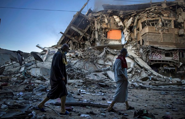 Palestinos caminham ao lado dos escombros de um prédio de 15 andares, atingido por ataques aéreos israelenses à cidade de Gaza, em 13 de maio de 2021.