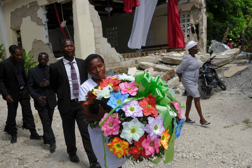 People carry a flower offering next to the earthquake-destroyed church where Baptist church minister Andre Tessono died, during his funeral in the Picot neighborhood in Les Cayes, Haiti, Sunday, Aug. 22, 2021, eight days after a 7.2 magnitude earthquake hit the area. People carry a flower offering next to the earthquake-destroyed church where Baptist church minister Andre Tessono died, during his funeral in the Picot neighborhood in Les Cayes, Haiti, Sunday, Aug. 22, 2021, eight days after a 7.2 magnitude earthquake hit the area.