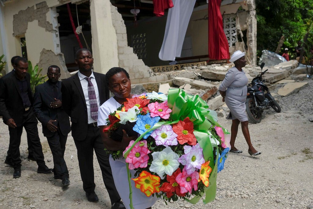 People carry a flower offering next to the earthquake-destroyed church where Baptist church minister Andre Tessono died, during his funeral in the Picot neighborhood in Les Cayes, Haiti, Sunday, Aug. 22, 2021, eight days after a 7.2 magnitude earthquake hit the area.