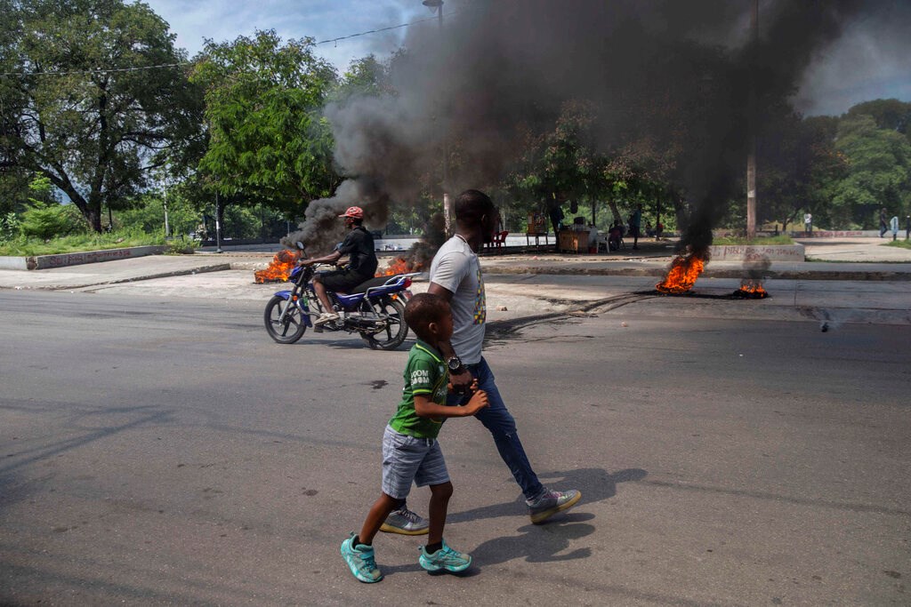 A man and a child walk by burning tires on a street in Port-au-Prince, Haiti on Sunday, October 17, 2021.